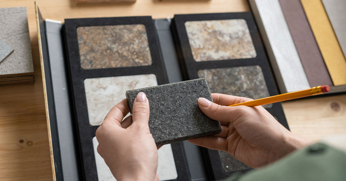 Person examining natural stone finish samples including granite and marble with different textures and finishes, illustrating the selection process for choosing natural stone finishes